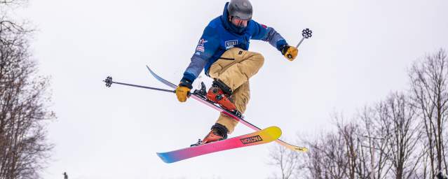 Skier performing a trick mid-air on colorful skis at Montage Mountain Ski Resort, surrounded by winter trees.