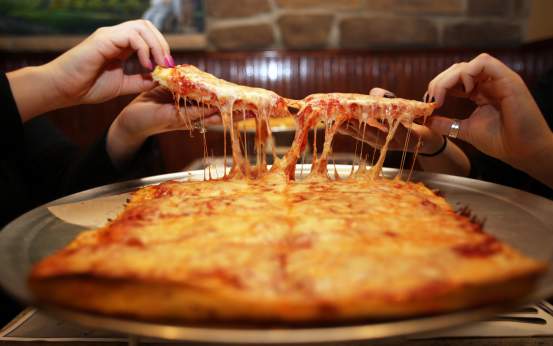 Two hands pull apart cheesy Old Forge pizza slices, with stretchy melted cheese from a golden-brown tray in Lackawanna County, PA.