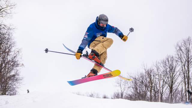 Skier performing a trick mid-air on colorful skis at Montage Mountain Ski Resort, surrounded by winter trees.