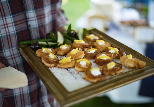 Catering service tray of small fried pastries topped with cream and yellow fruit slices, held by a person in a plaid shirt.