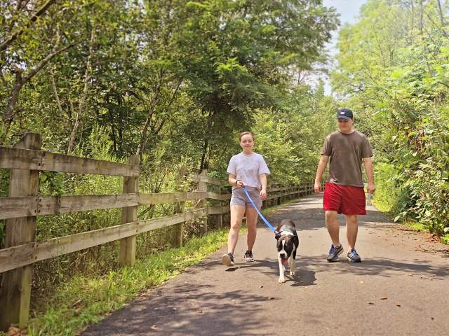A man and woman walking a dog along the Lackawanna River Heritage Trail