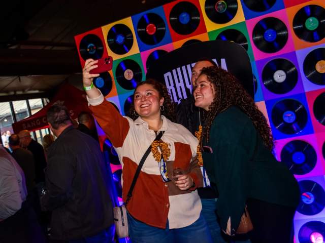 Three friends taking a selfie in front of a Rhythm & Brews decorative wall at the Rhythm & Brews festival at Montage Mountain Resorts in Scranton, PA
