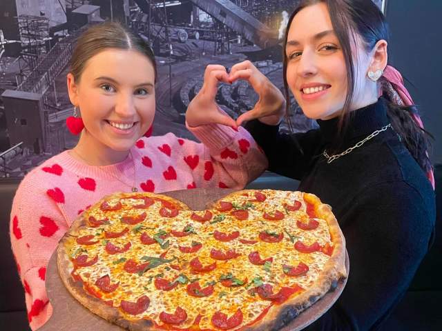 Two women holding a heart-shaped pizza from Colarusso's Coal Fired Pizza