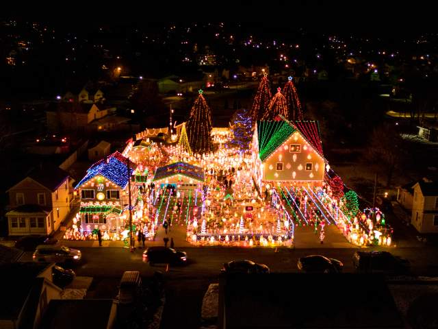 Aerial nighttime view of Peckville, PA neighborhood with colorful Christmas lights, decorated houses, and illuminated trees during the holiday season.