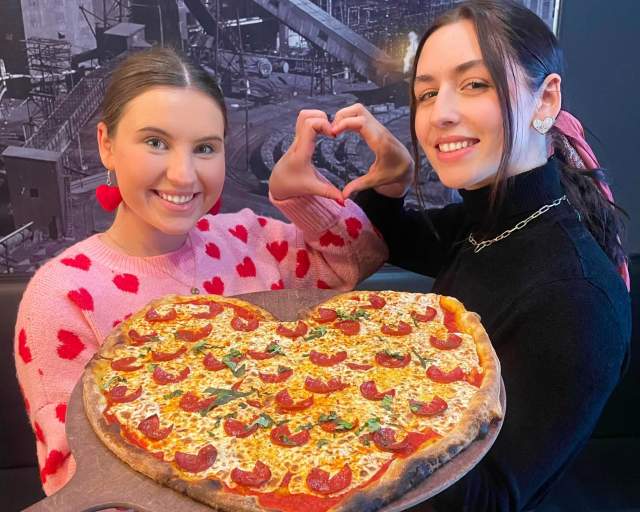 Two women holding a heart-shaped pizza from Colarusso's Coal Fired Pizza