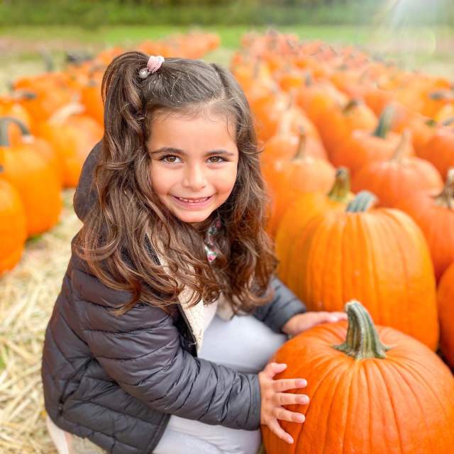A child posing with a pumpkin at Ritter's Cider Mill