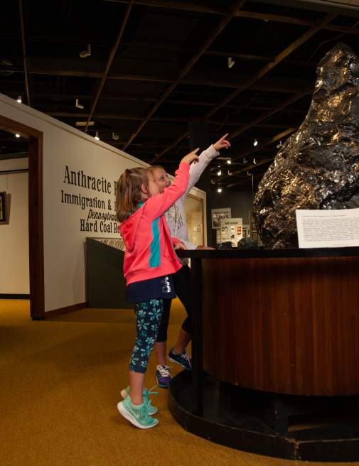 Two children pointing at a large piece of anthracite on display at the Anthracite Heritage Museum in Scranton, PA