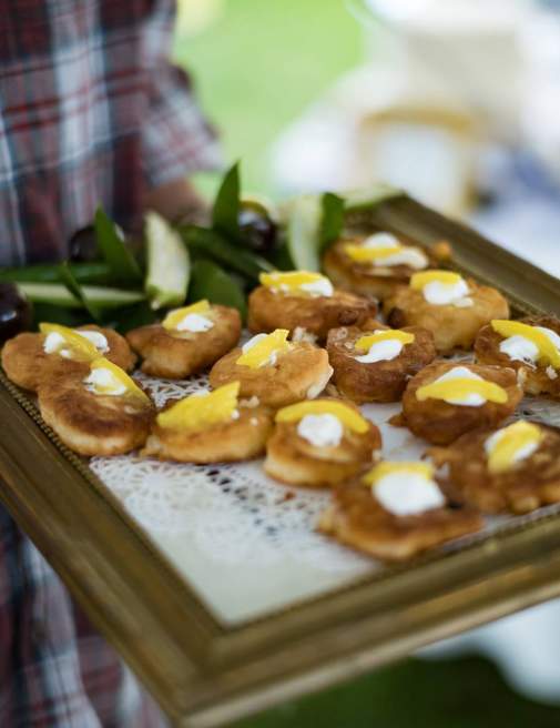 Catering service tray of small fried pastries topped with cream and yellow fruit slices, held by a person in a plaid shirt.