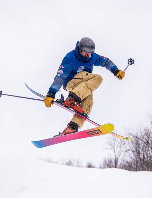 Skier performing a trick mid-air on colorful skis at Montage Mountain Ski Resort, surrounded by winter trees.