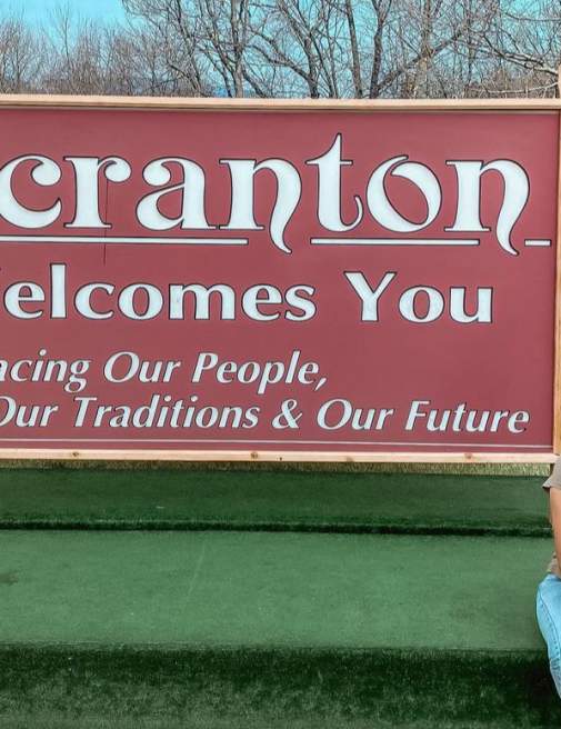 woman sitting in front of Scranton Welcomes You Sign in Downtown Scranton, PA