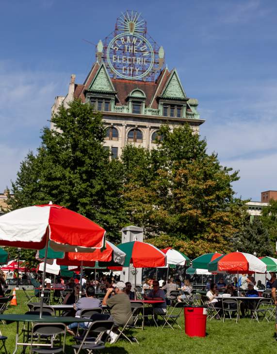 Tables with Italian-colored umbrellas in Courthouse Square in front of the Electric City Sign