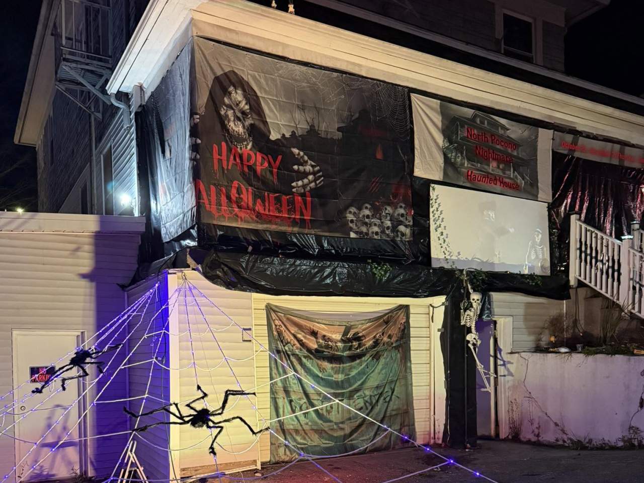 North Pocono Place Haunted House decorated with giant spiders, glowing webs, skeletons, skulls, and spooky Halloween banners at night.