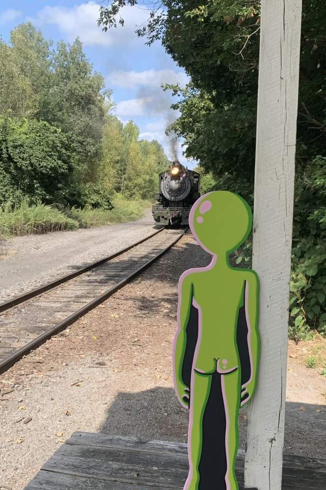 An "alien" standing alongside the railroad tracks as a steam train approaches to head to the Carbondalien Festival in Carbondale, PA