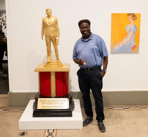A man posing for a photo with the Dundie Award near The Office Exhibition at the Everhart Museum in Scranton, PA