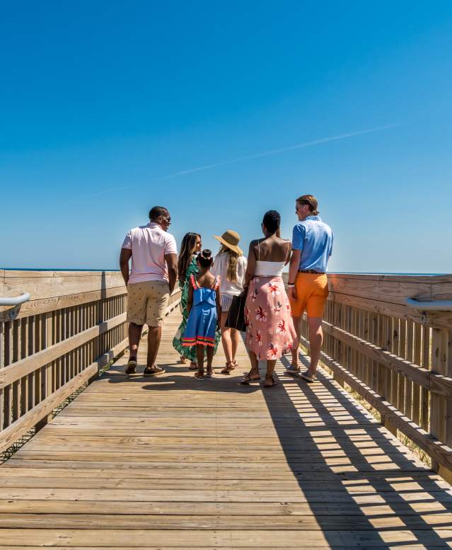 People walking on a boardwalk on a sunny day under a clear blue sky.