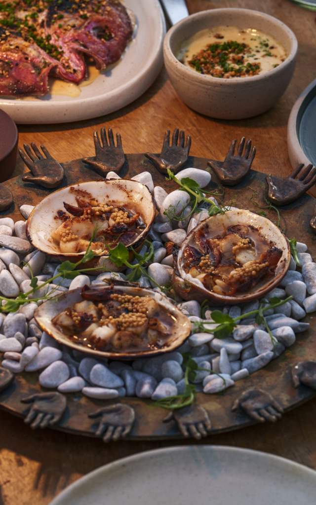 A table adorned with seafood dishes, including clams on a decorative platter, surrounded by drinks and other plates