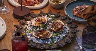 A table adorned with seafood dishes, including clams on a decorative platter, surrounded by drinks and other plates
