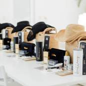 Bachelorette party gift bags and personalized swag, including straw hats and tumblers, arranged on a long white table.