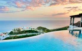 A stunning infinity pool at Casa Stella reflecting the vibrant pink and orange colors of a Los Cabos sunset.