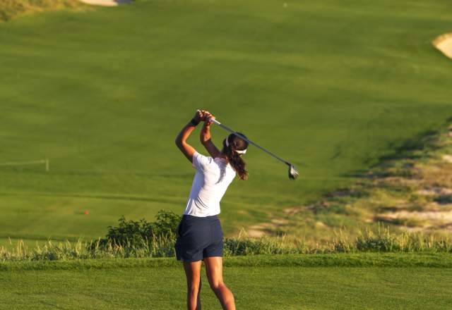 A female golfer making a swing with an ocean view