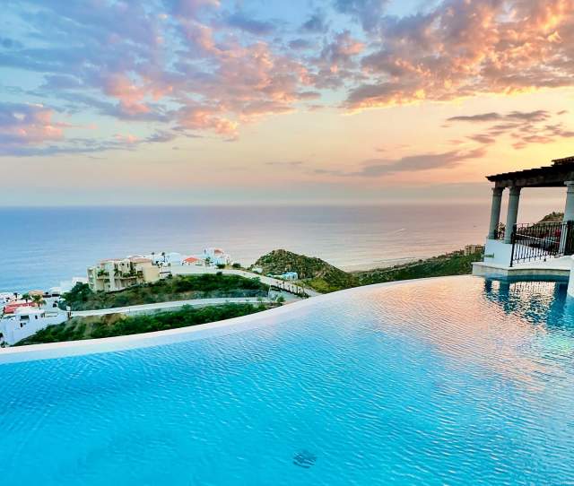 A stunning infinity pool at Casa Stella reflecting the vibrant pink and orange colors of a Los Cabos sunset.