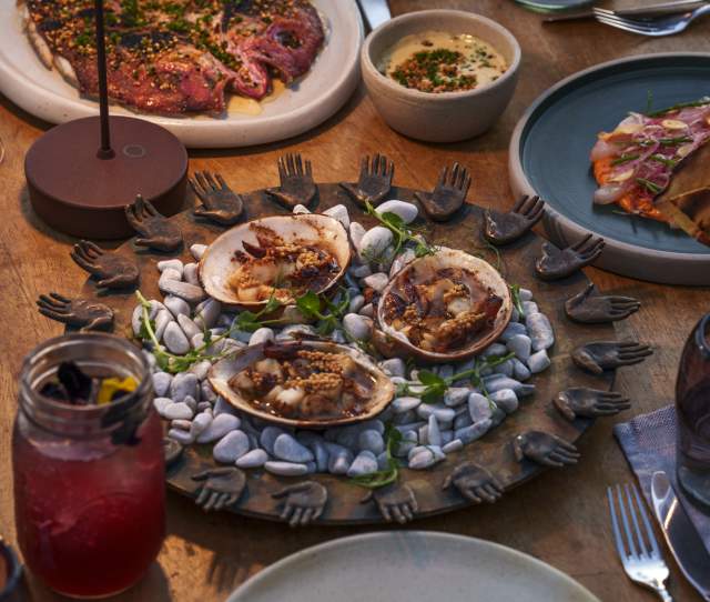 A table adorned with seafood dishes, including clams on a decorative platter, surrounded by drinks and other plates