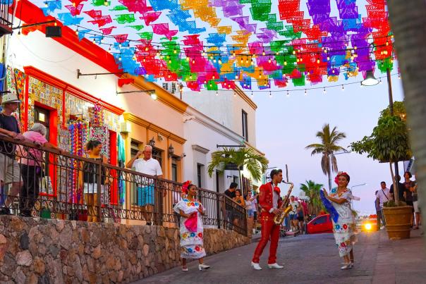 Traditional dancers and a musician perform under vibrant papel picado banners during the San José del Cabo Art Walk.