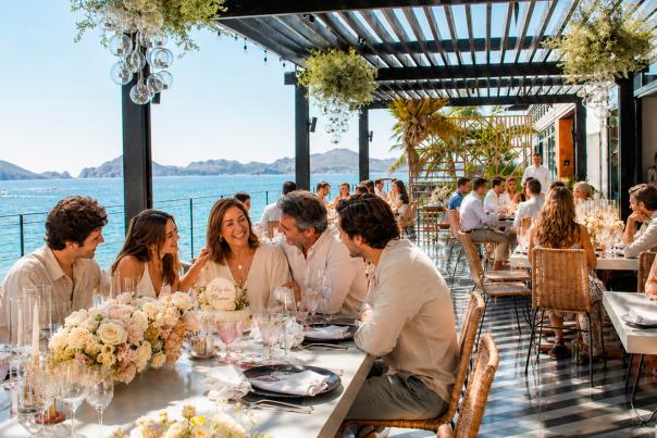 Familia celebrando el Día de las Madres durante un brunch frente al mar en Los Cabos, con una madre como protagonista acompañada de sus hijos y esposo en un restaurante con ambiente elegante y relajado.