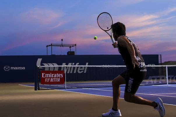 Jugador profesional de tenis golpeando una pelota de tenis al atardecer