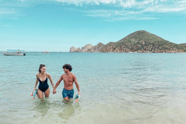 Pareja heterosexual tomada de la mano saliendo del mar de cortés