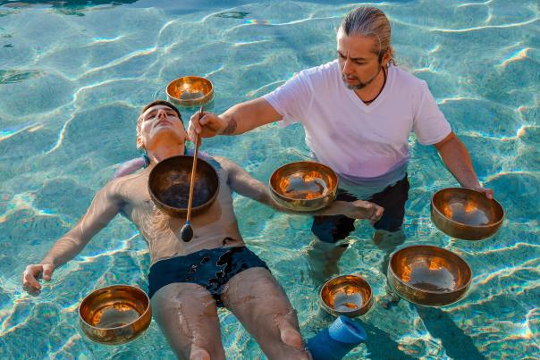 hombre en la alberca haciendo terapia de sonido con cuencos tibetanos en el agua