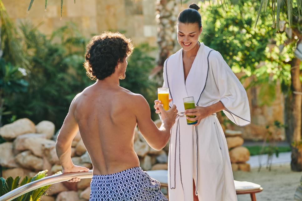 pareja heterosexual saliendo de la piscina con jugos en la mano