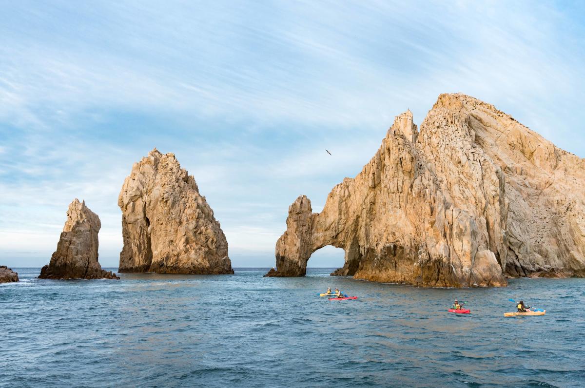 A small group of people paddling in a kayak towards the Arch of Cabo San Lucas in Los Cabos, Mexico
