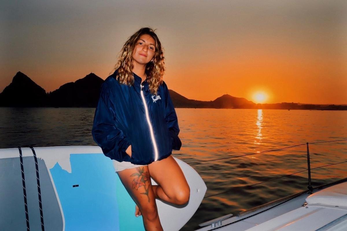 Fotografía de Karen recargada en una tabla de surf con el fondo del mar al atardecer