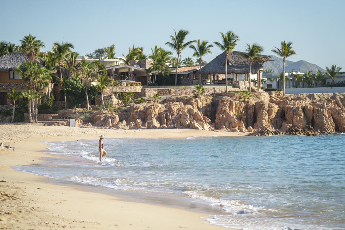 A serene beach with golden sand, calm waves, and luxury beachside villas shaded by palm trees in the background.