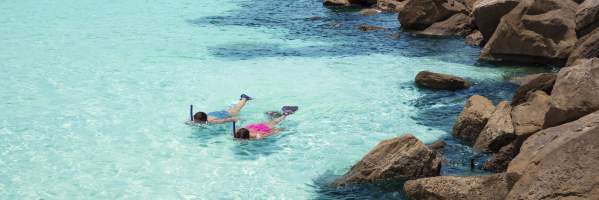 Two adults snorkeling near a rocky shore