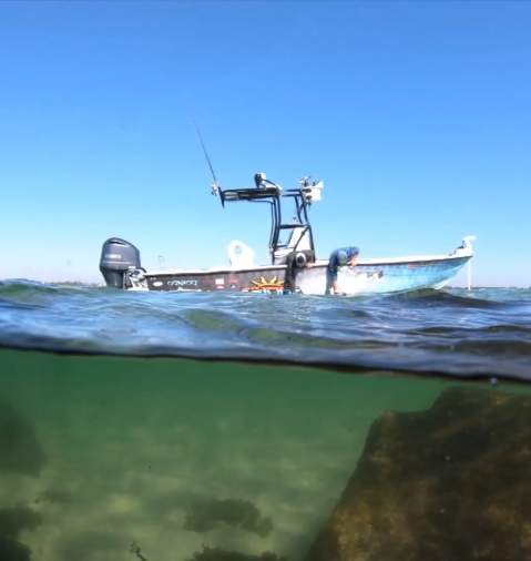 wo men reaching into the ocean water from their anchored fishing boat
