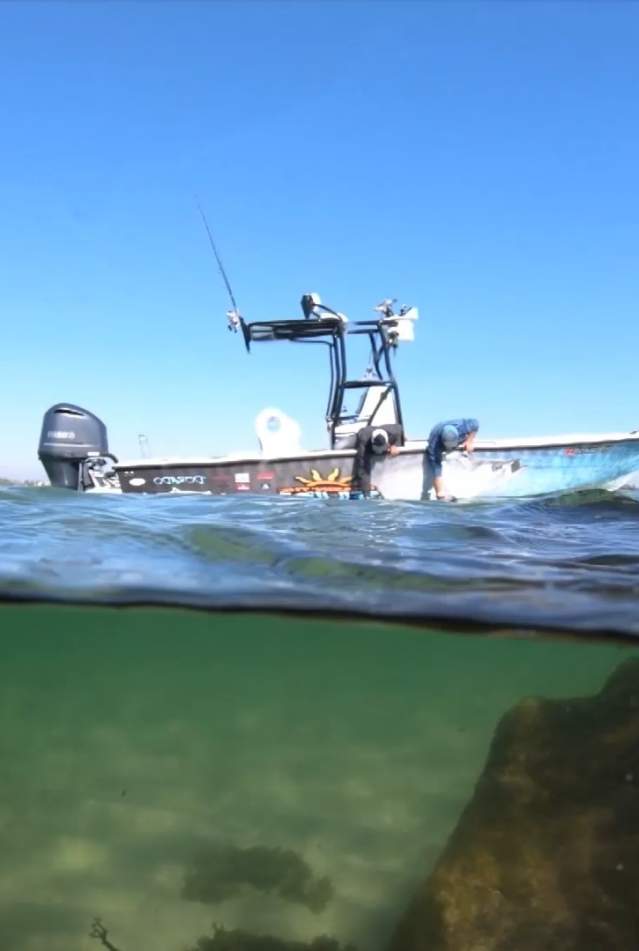 wo men reaching into the ocean water from their anchored fishing boat