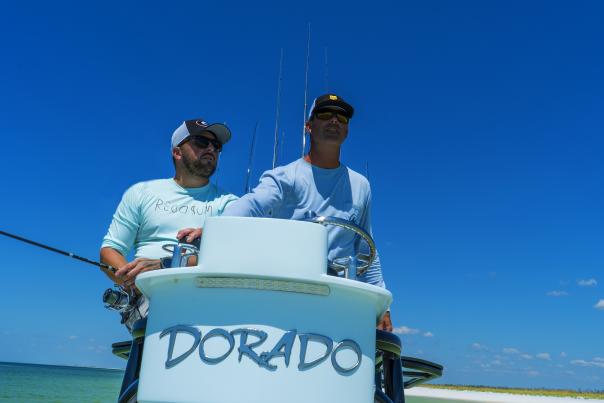 Two men headed out on fishing boat that says "Dorado"
