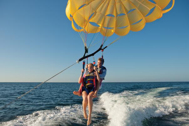 Two people parasailing just above foamy water