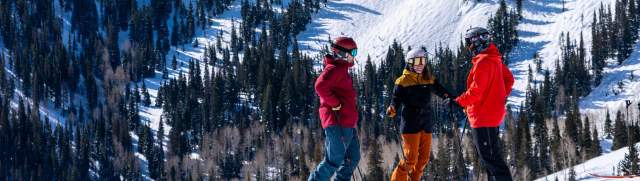 Three skiers discuss a run in front of tall mountains at Deer Valley in Park City, UT