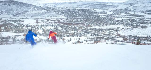 Two people skiing at Park City Mountain with a view of the town in the background