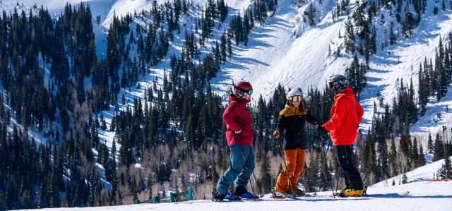 Three skiers discuss a run in front of tall mountains at Deer Valley in Park City, UT
