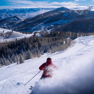 A skier carves a turn on a powder run on clear and sunny day in Park City, UT