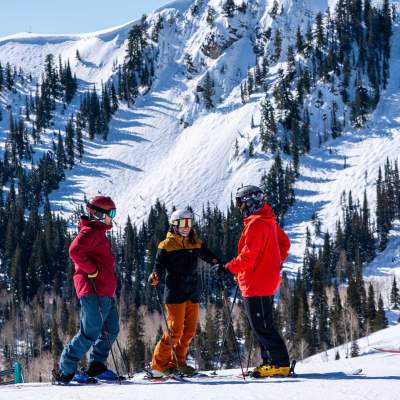 Three skiers discuss a run in front of tall mountains at Deer Valley in Park City, UT