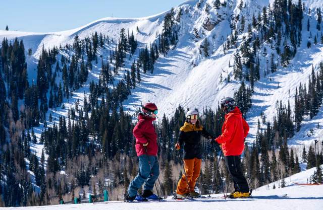 Three skiers discuss a run in front of tall mountains at Deer Valley in Park City, UT