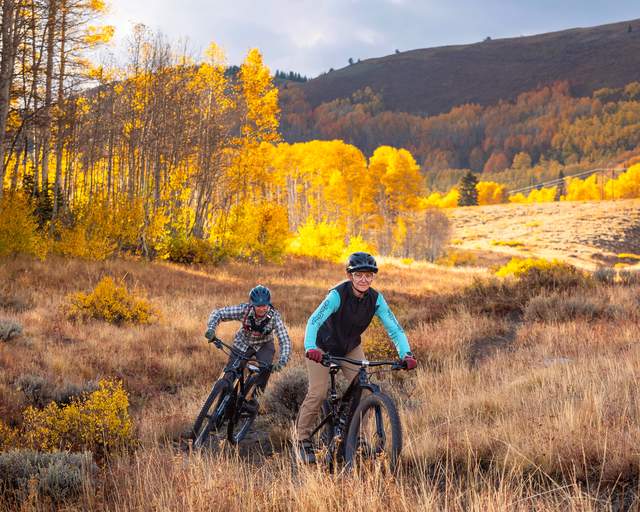 Two mountain bikers ride across an alpine meadow surrounded by colorful fall leaves near Park City, UT