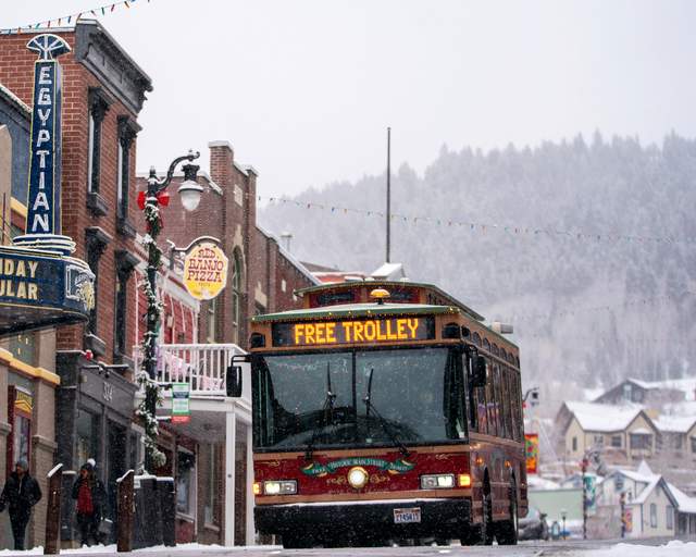 A trolley drives down Historic Main Street adorned with festive decorations on a snowy day in Park City, UT