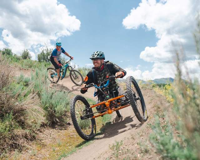 An adaptive mountain biker rides on a wide trail in Round Valley in Park City, UT