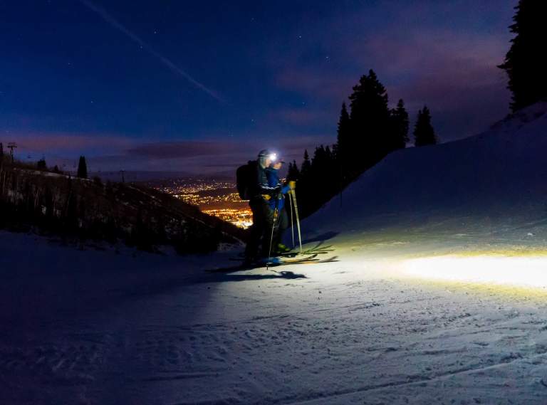 Two skiers tour on the approved route up Park City Mountain at night with headlamps